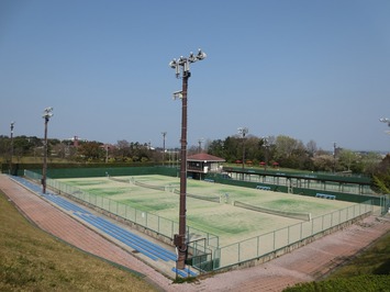 側面に照明を2基備えた4面からなるテニスコートを斜め上から撮影した写真