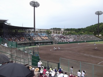 観客が見守る内野席から試合中のホームベースを右側から撮影した写真