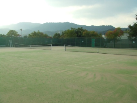 遠くに雲がかかった山が見える、緑に囲まれた美保関総合運動公園テニスコートAコートとBコートの写真。
