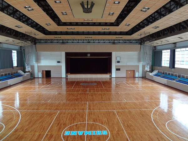 天井の照明が点灯していてバスケットコートが2面、左右に青色の客席が設置された島根町民体育館の大体育館の内観写真