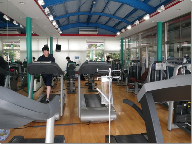 アーチ状の屋根と緑の柱とランニングマシンが複数台置かれたトレーニングルームで、利用者がランニングマシンを使用している様子を撮影した写真