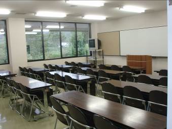 1個の教卓とその前に12個の茶色い長机と32脚のパイプ椅子が設置されたサンライフ松江の研修室の写真