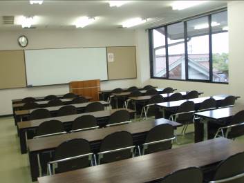 天井の蛍光灯が点灯している室内に1個の教卓と11個の長机と30脚のパイプ椅子が設置されたサンライフ松江の研修室の写真