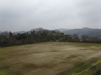 くもり空の下、空口公園多目的広場のグラウンドの写真、奥には山や木々が見える