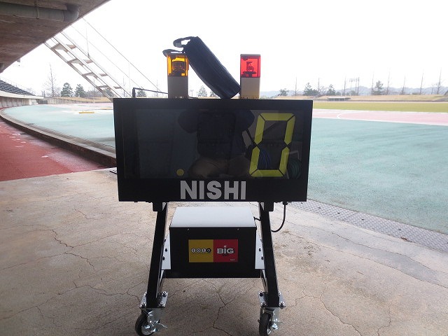 移動用の4つのタイヤが付いた黒い筐体に、数字の入った表示板と黄色と赤の二つのライトが上に備えられたタイマーの写真