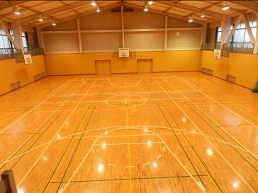 天井からつるされた照明が点灯しているバスケットボールのコートが写った松江市矢田体育館の内観写真、奥にバスケットゴールが3基写っている