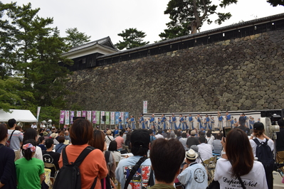松江城の生垣の下にあるステージでの演舞を大勢の観客が見ている写真