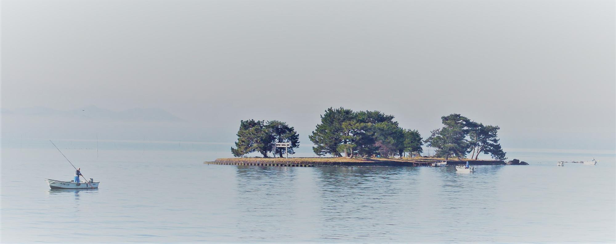 広い海に小さな島がポツンとあり、小舟が2隻見える写真