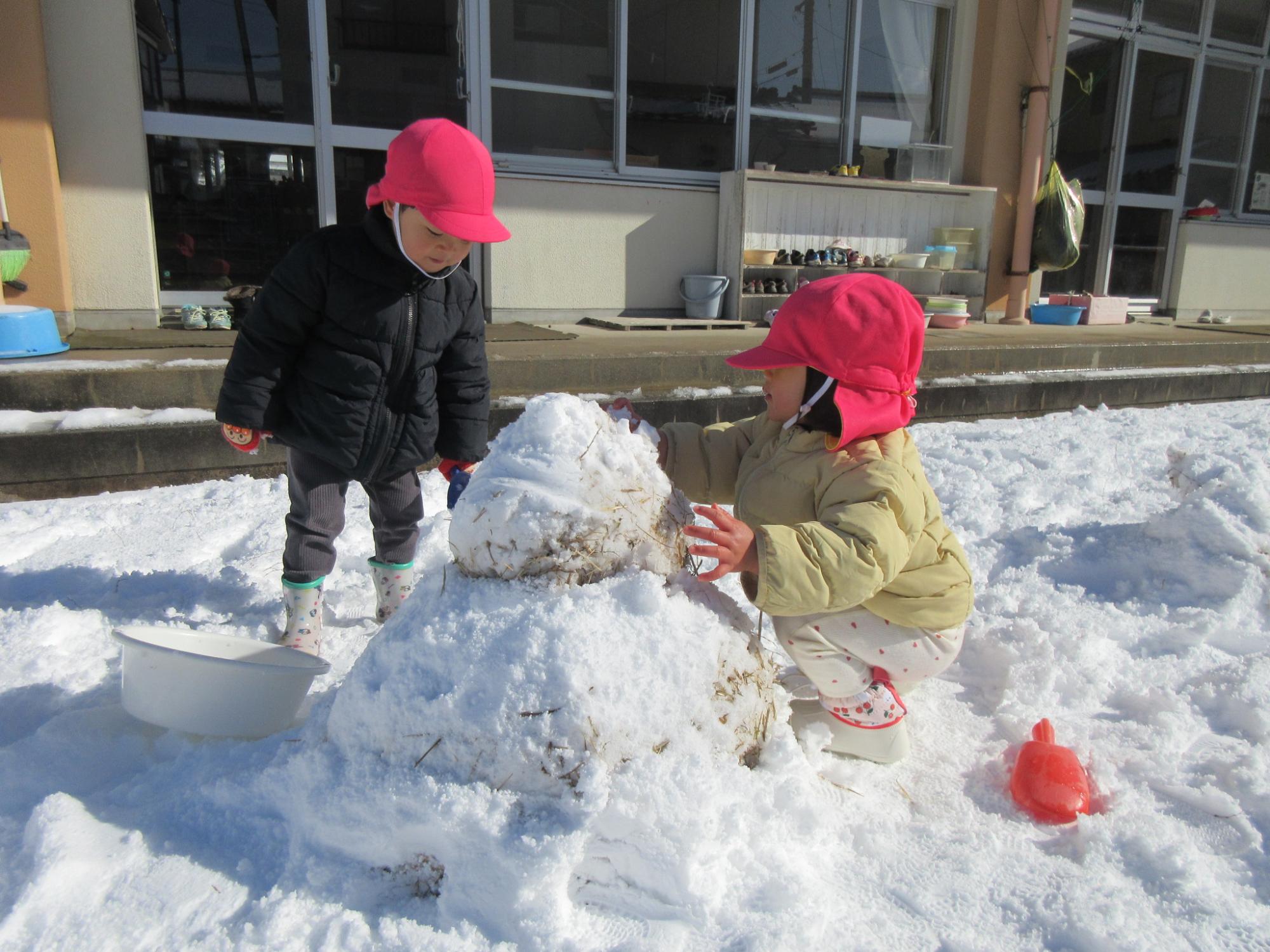 裏庭で小さい雪だるまを作る男の子と女の子