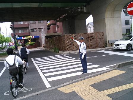 横断歩道で自転車で通学している生徒たちに街頭指導をしている写真