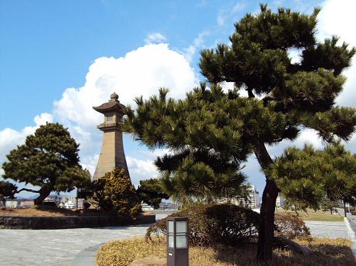 青い空の下、松の木の間から奥の灯篭が見える風景写真