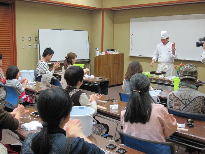 前に立って和菓子作りの説明をする男性の職人と、真剣に作っている受講者の写真