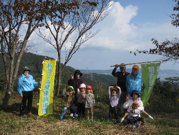 山の頂上で中海を背景に記念撮影をする朝酌健康推進隊と園児