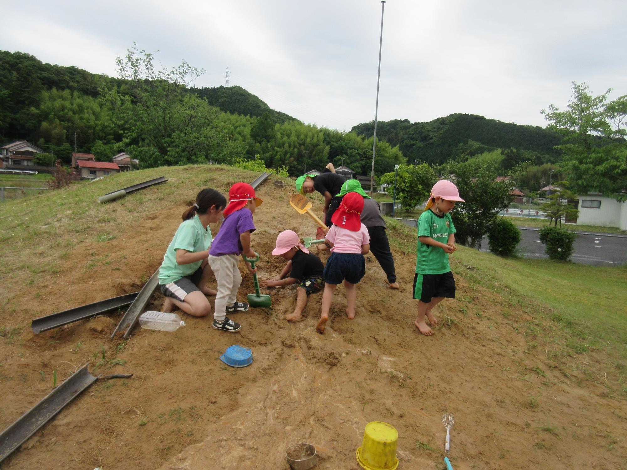 こどもたち先生が築山でスコップで穴を掘って遊んでいます。
