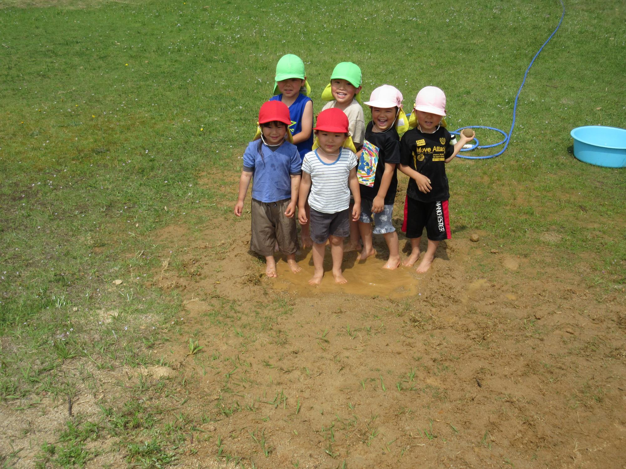 6人のこどもたちがどろんこプールにみんなで入ってこちらを向いて笑っている