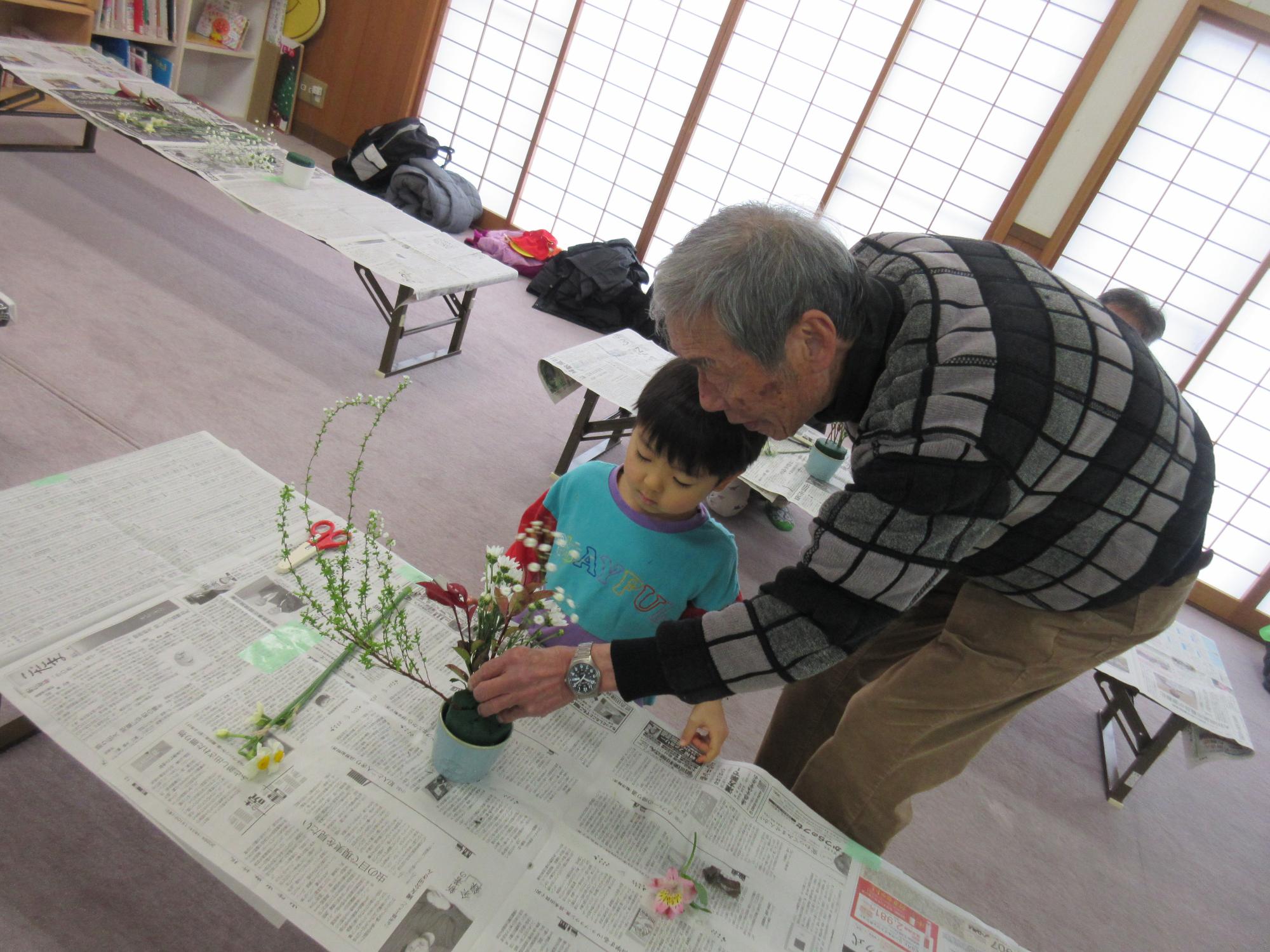 公民館での生け花教室で、園児がお花の先生に花のさし方教えてもらっている