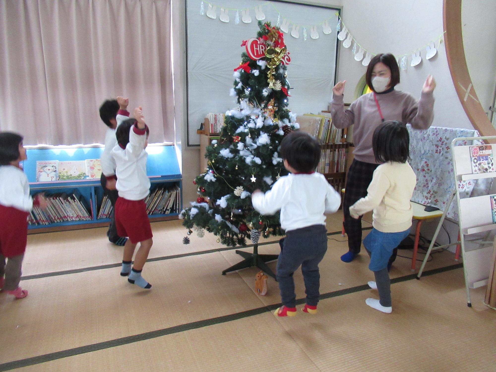 飾りつけしたツリーの周りで、先生と子どもたちがとびあがって喜んでいます。