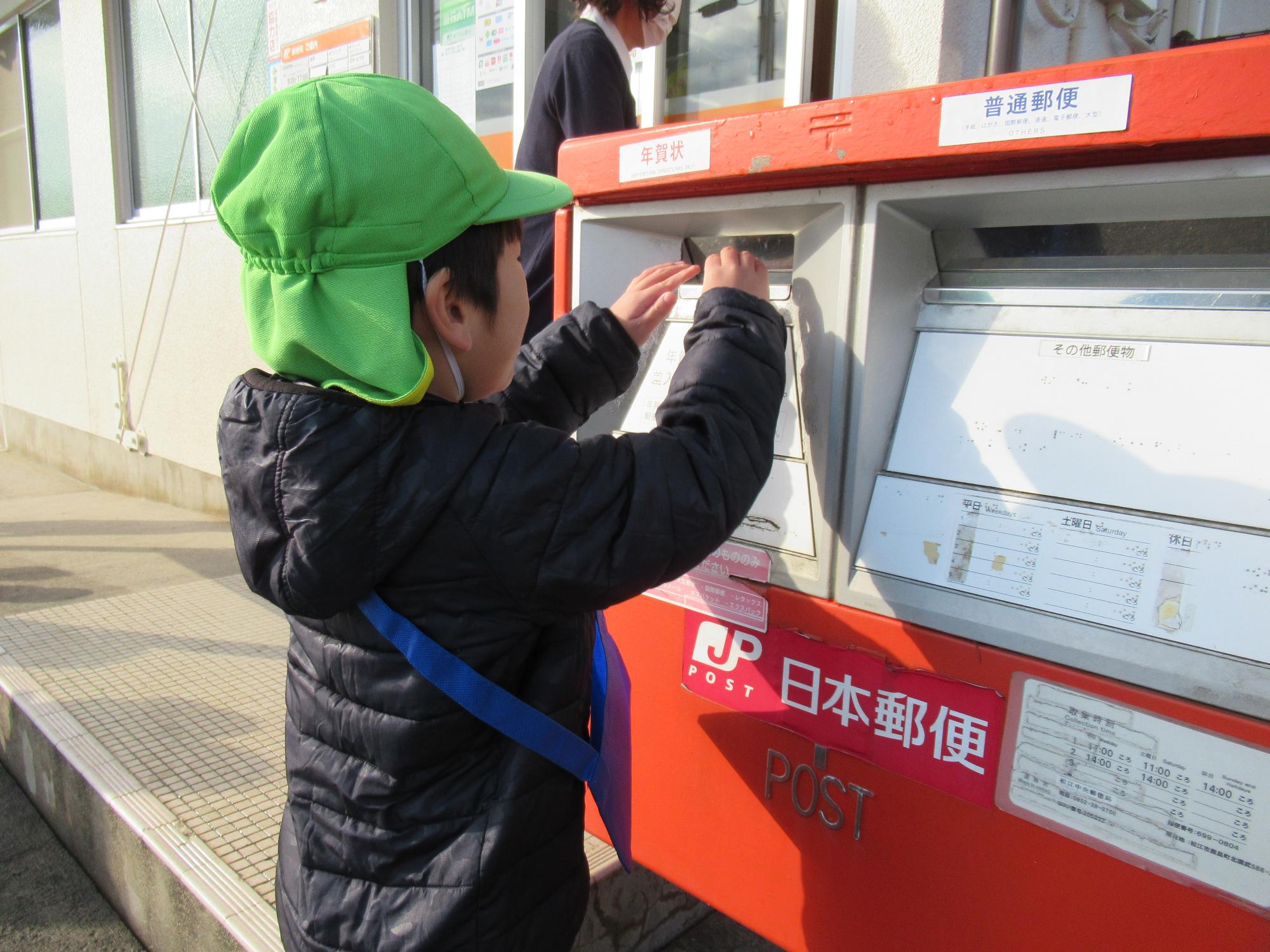 おうちの人に書いた年賀状をポストに投函する子ども。