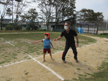 リレーの練習の折、スタート地点でバトンを待つ園児と校長先生の写真