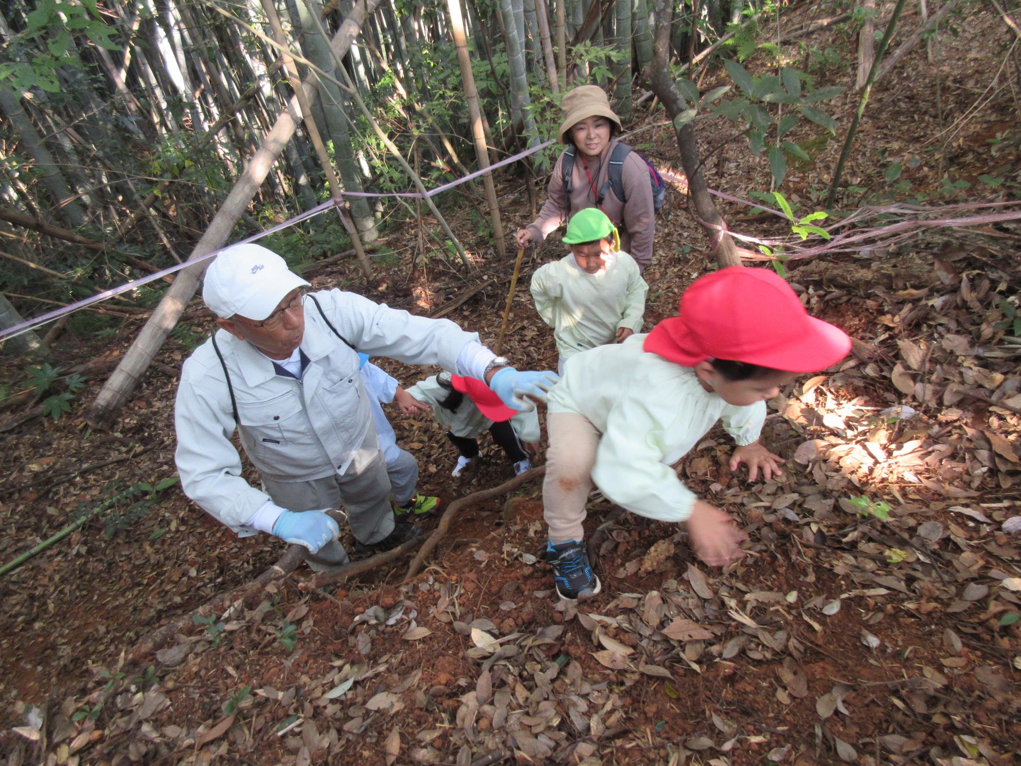 子どもが、園長先生に支えてもらいながら崖のぼりに挑戦しています。