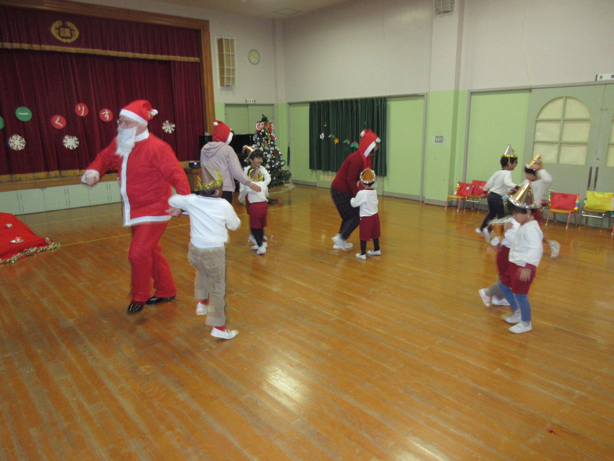 クリスマス会でサンタさんと子どもたちが楽しくダンスを踊っています。