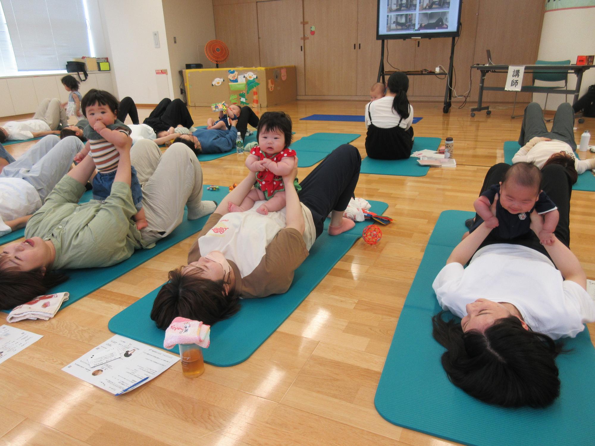 子育て学習会で赤ちゃんを抱っこしながらストレッチを行う参加者