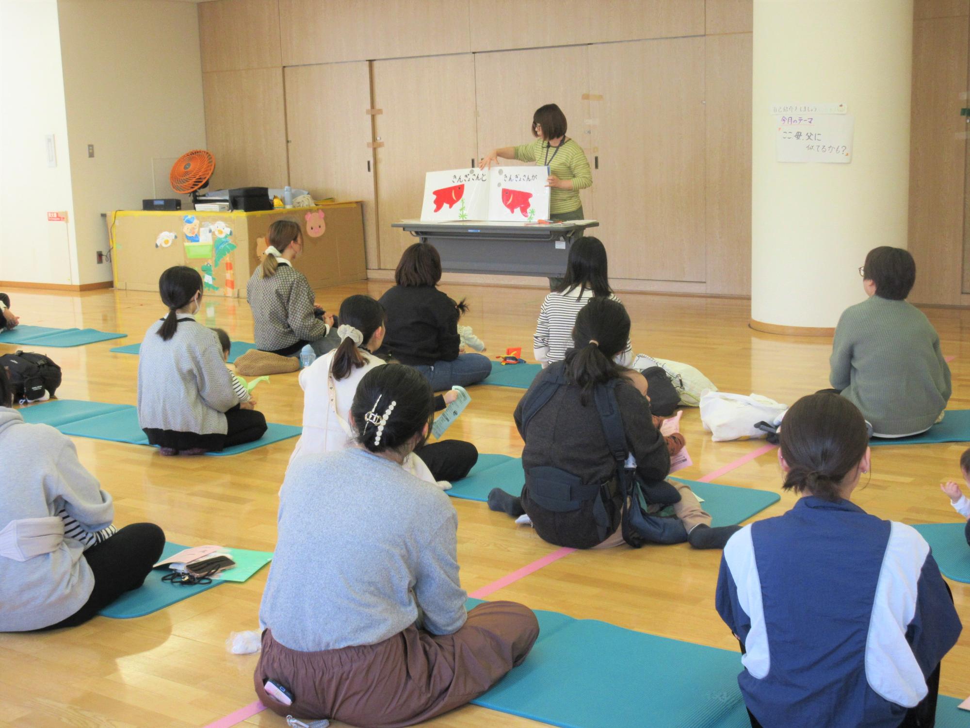 母の膝の上や抱っこで、大型絵本だるまさんがの読み聞かせを聞いている様子