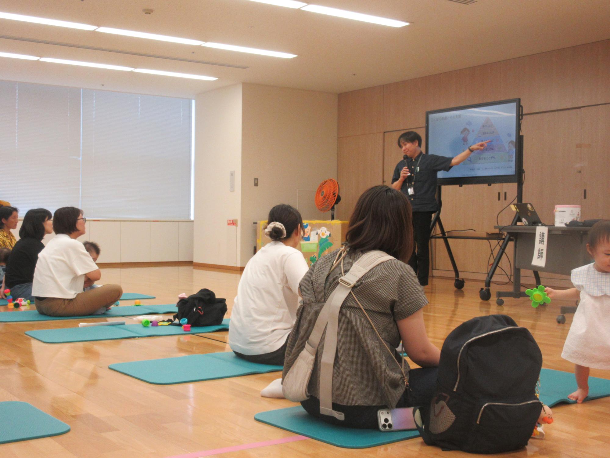 子育て学習会で電子黒板を指さしながら話す水内先生の話を聞く様子
