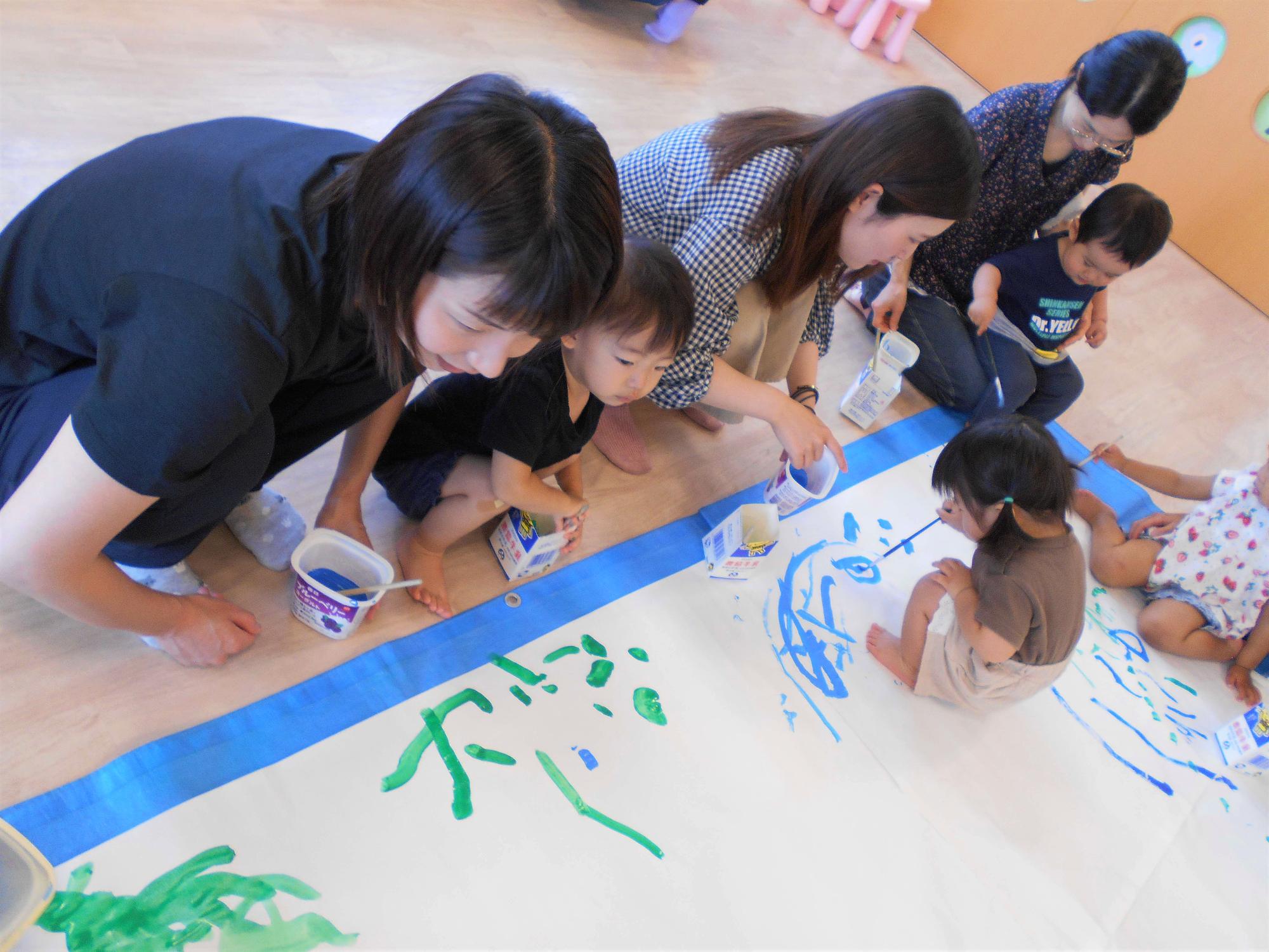 つどいで、親子で大きな紙にお絵描きを楽しんでいる様子