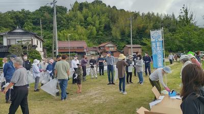 山林の住宅付近にある芝の広場でゴミ拾いをしている人たちの写真