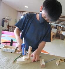 黒いマスクをした少年が工具を使って木製の作品を作っている写真