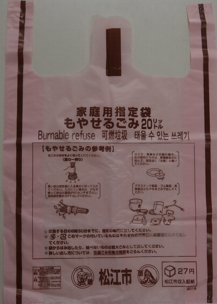 持ち手のついた松江市指定ごみ袋。さくら色の袋に、茶色の文字で家庭用指定袋もやせるごみ20リットルと書かれている。