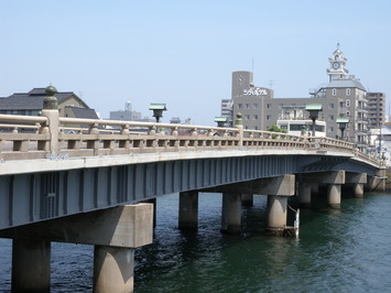 遠くに小さく見える松江城を背景に、青空の下に広がる松江大橋の写真