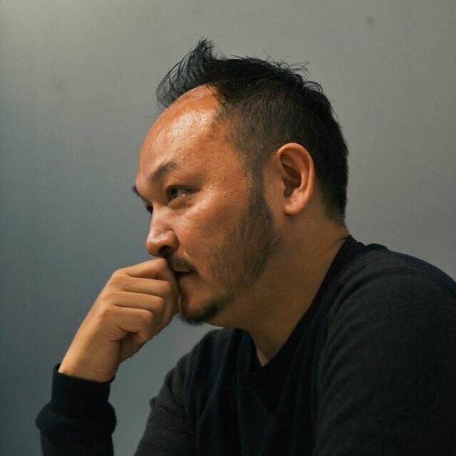 右手を口元に当てている大島芳彦さんを左側から写した写真