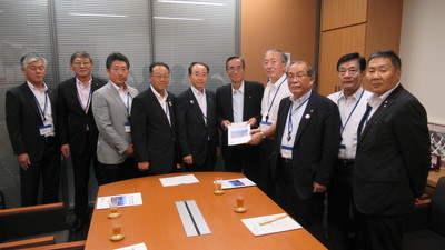 10名の男性が横一列に並び、中央に立つ細田博之衆議院議員と同盟会の男性が一緒に要望書を持っている集合写真