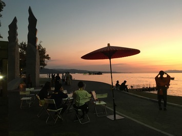 夕焼けで赤く染まっている空の下、遊歩道沿いに沢山の人たちが集まり楽しんでいるミズベリング縁日の様子の写真