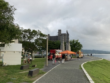 海が見える遊歩道沿いにキッチンカーが間隔を開けて駐車している岸公園の写真