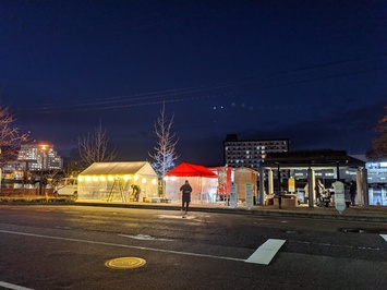 白色と赤色のテントの中が照明で明るく照らされた屋台を道路の反対側から撮影した写真